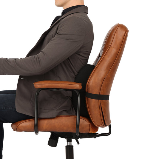Close-up of a black memory foam lumbar support pillow strapped to a modern office chair with sunlight streaming through a nearby window.